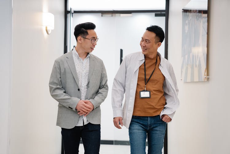 Man In Gray Blazer Talking To Man In Striped Shirt With Badge Standing Beside