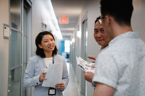 Free Three business professionals discussing teamwork strategies in a modern office hallway. Stock Photo