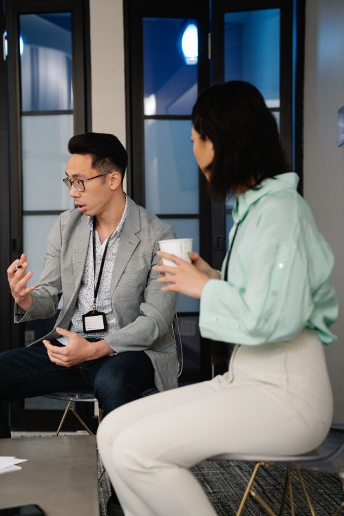 Free Two professionals engage in a focused discussion over coffee in a modern office environment. Stock Photo