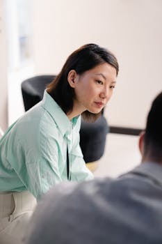 Asian woman in a business meeting, wearing a light green shirt, engaged in a discussion.