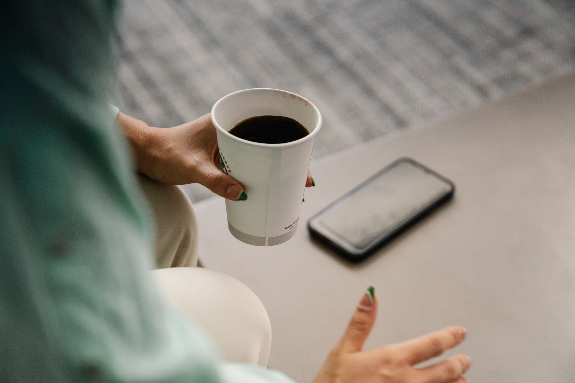 Best gratitude apps for your phone: top picks for daily gratitude Woman holding a paper coffee cup with smartphone nearby in a relaxed setting.