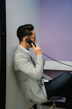 Businessman engaged in a phone call, wearing glasses and blazer indoors.