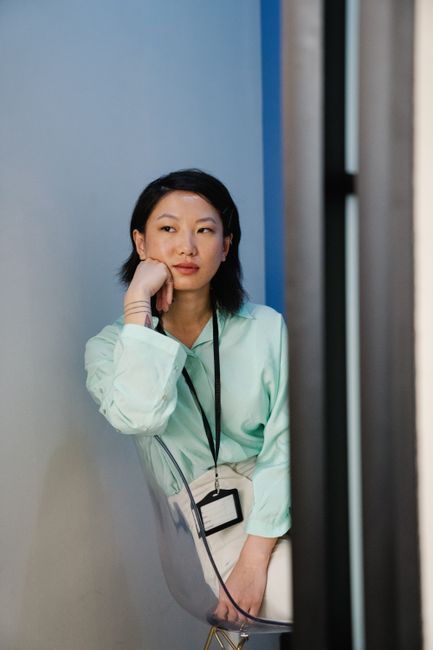 An adult woman in a mint green shirt reflects while leaning against a wall in an indoor setting.