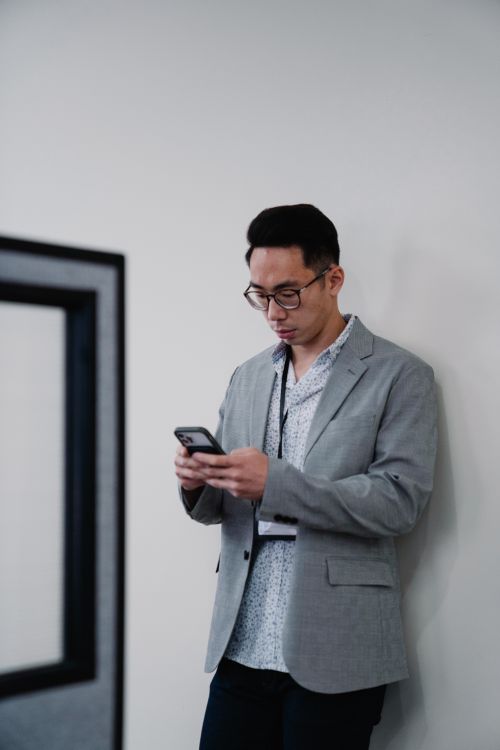 Free Young professional man in office attire using smartphone, focused and engaged. Stock Photo