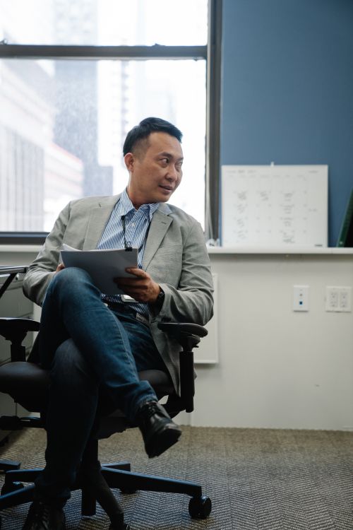 Free Asian man sitting in an office chair holding a document, looking attentive. Stock Photo