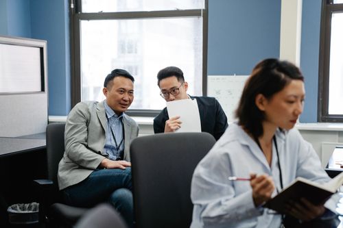 Free Colleagues whispering during work in an office setting, signaling teamwork and collaboration. Stock Photo