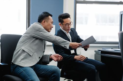 Free Two male colleagues exchanging documents in a modern office setting. Stock Photo
