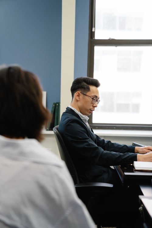 Free Young Asian man working at a desk in a modern office, seated in business attire with a laptop. Stock Photo