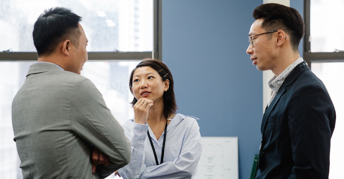 Three business colleagues engage in a thoughtful discussion in a modern office setting.