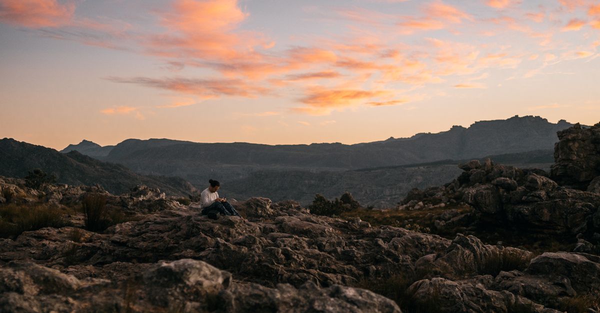 person sitting on a mountain top looking at the sunset, peaceful expression