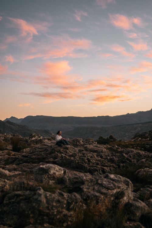 Free A person sits contemplatively among rocky terrain at sunset, embracing tranquility in nature. Stock Photo