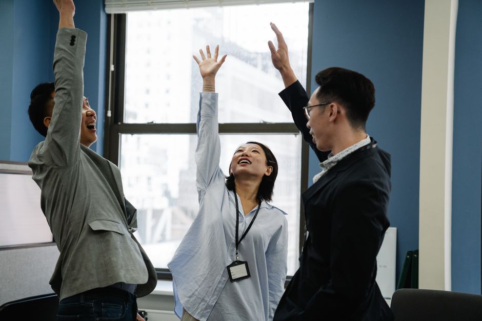 多様な同僚3人がハイタッチし、現代的なオフィス環境での成功を祝っています。