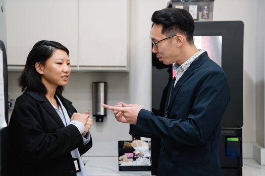 Two coworkers engaged in a conversation in a modern office break room.