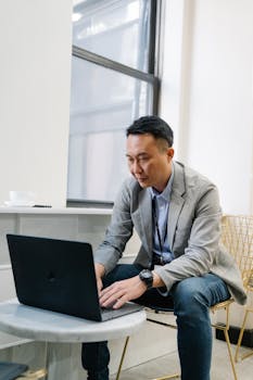 Asian business professional working on laptop in modern office setting.