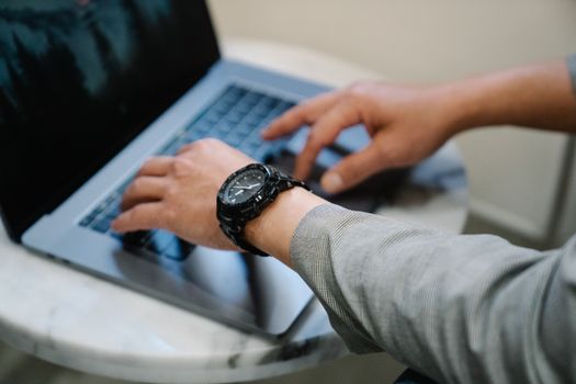 A person in business attire typing on a laptop, wearing a wristwatch, in a professional setting.