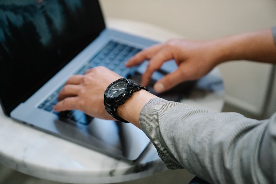A person in business attire typing on a laptop, wearing a wristwatch, in a professional setting.