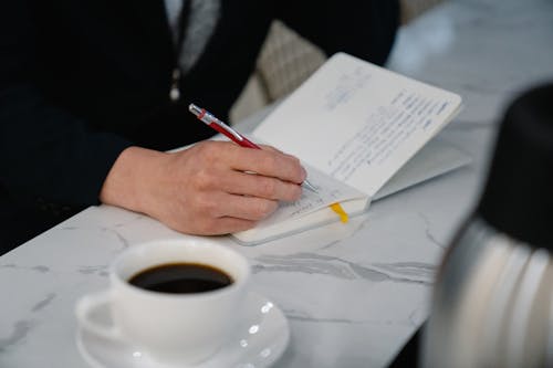 Close-up of a Man Writing in His Calendar and Drinking Coffee 