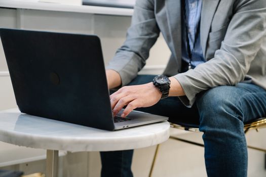 A focused man typing on a laptop in a modern office environment, showcasing casual work attire.