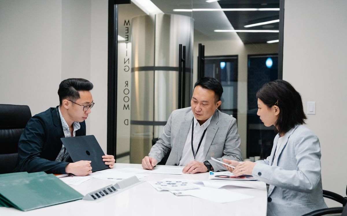 Business meeting with three professionals collaborating in a modern conference room setting.
