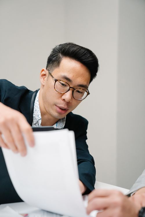 Free Asian man in eyeglasses examining papers in an office setting. Stock Photo