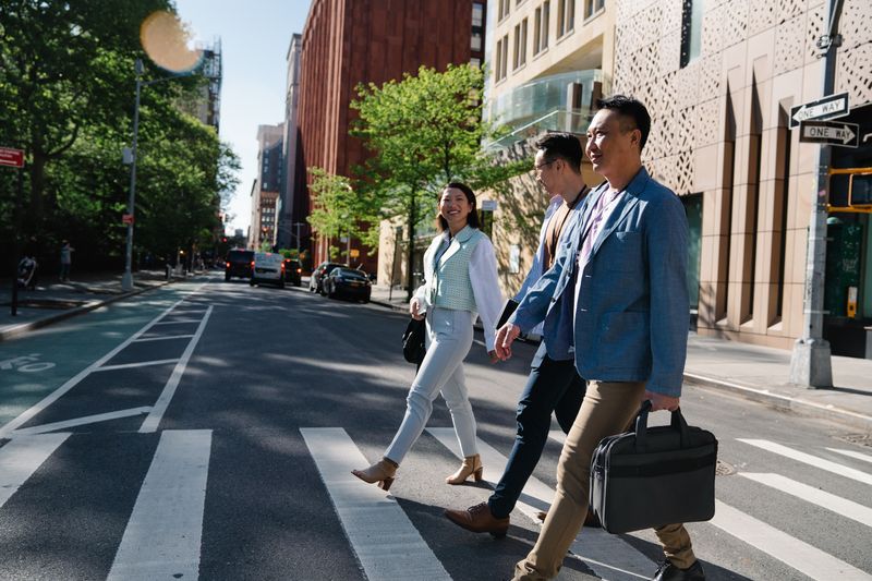 A group of business professionals crosses a city street