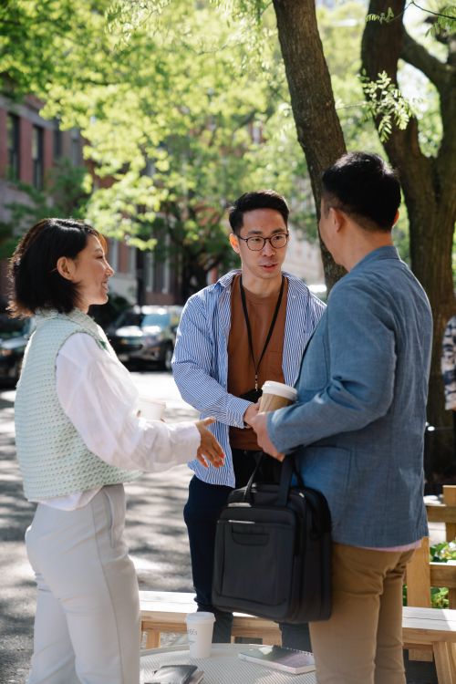 Free Three adults engaged in a friendly business meeting outdoors, shaking hands under green trees on a city street. Stock Photo