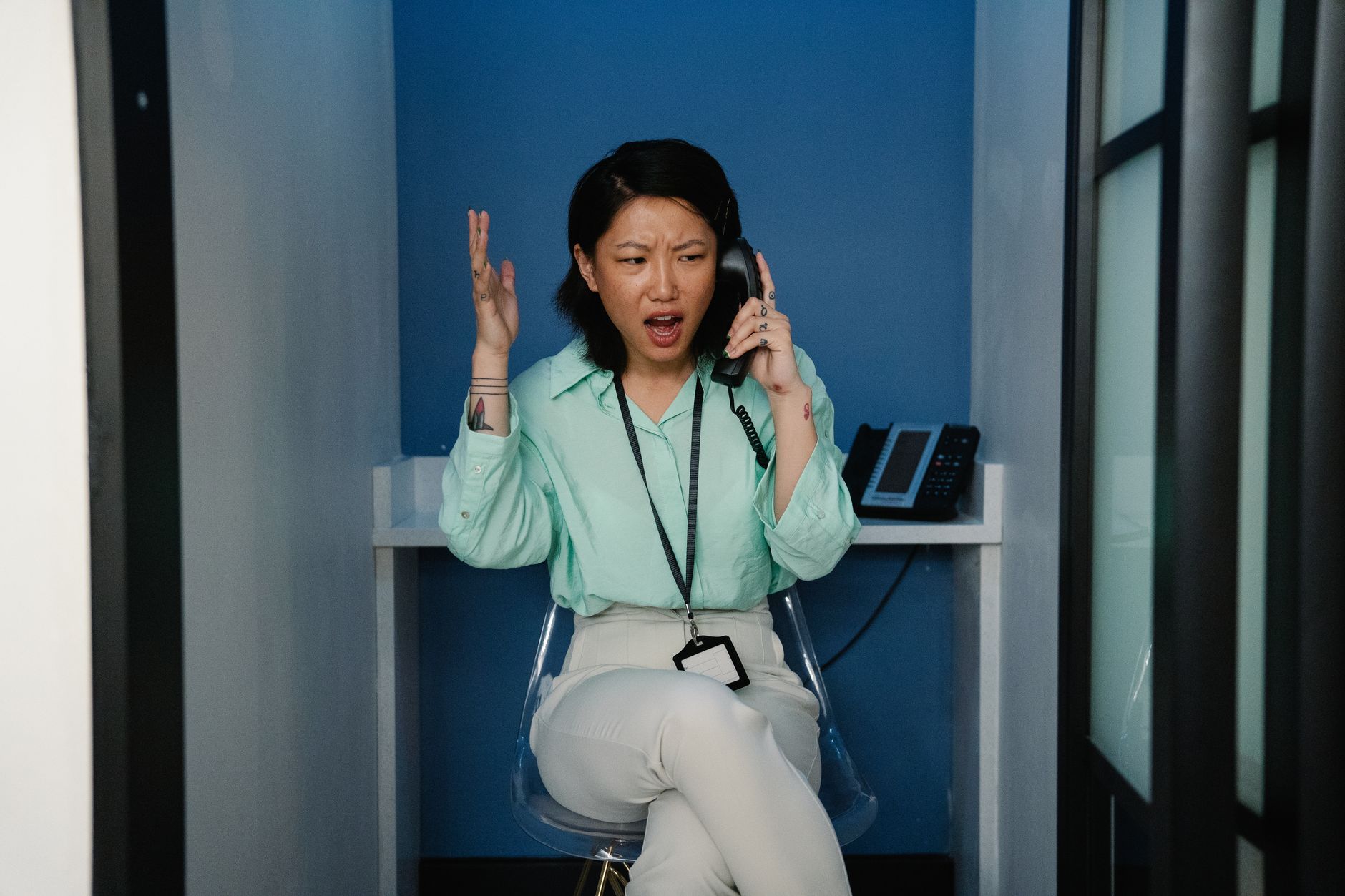 An east Asian woman expressing frustration during a phone call at the workplace.