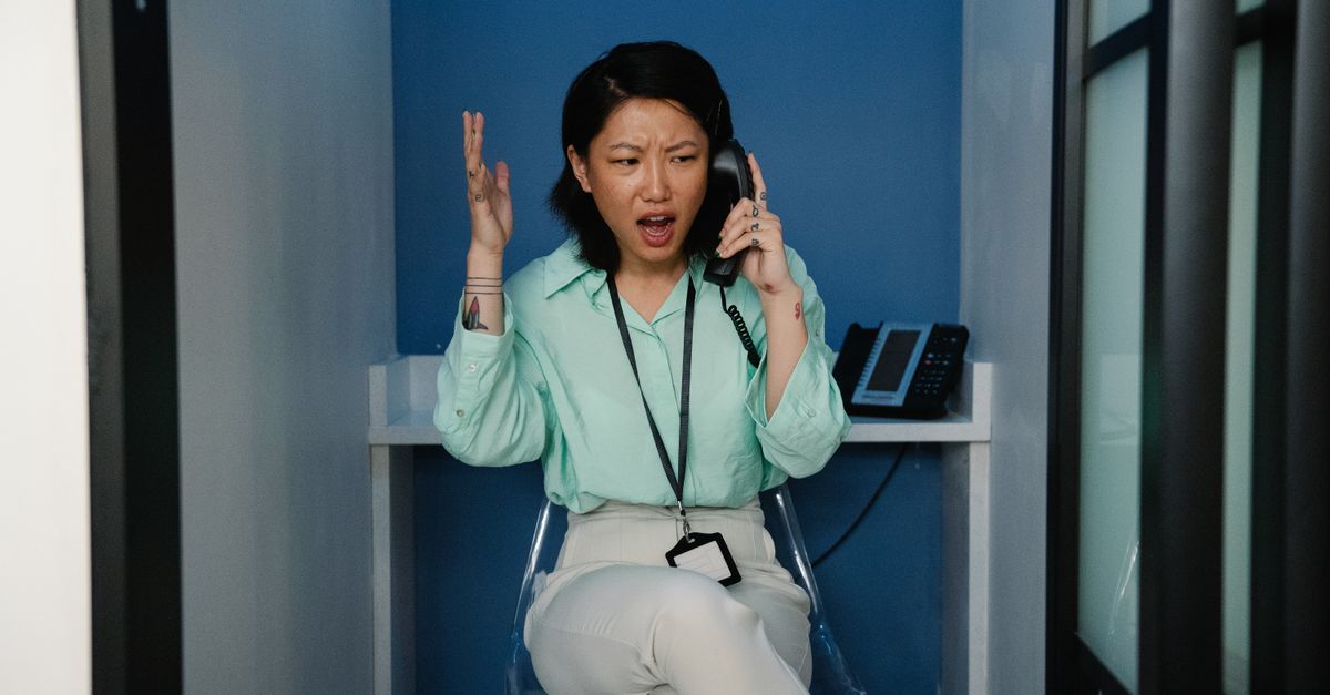 person sitting at messy desk with phone in hand looking stressed