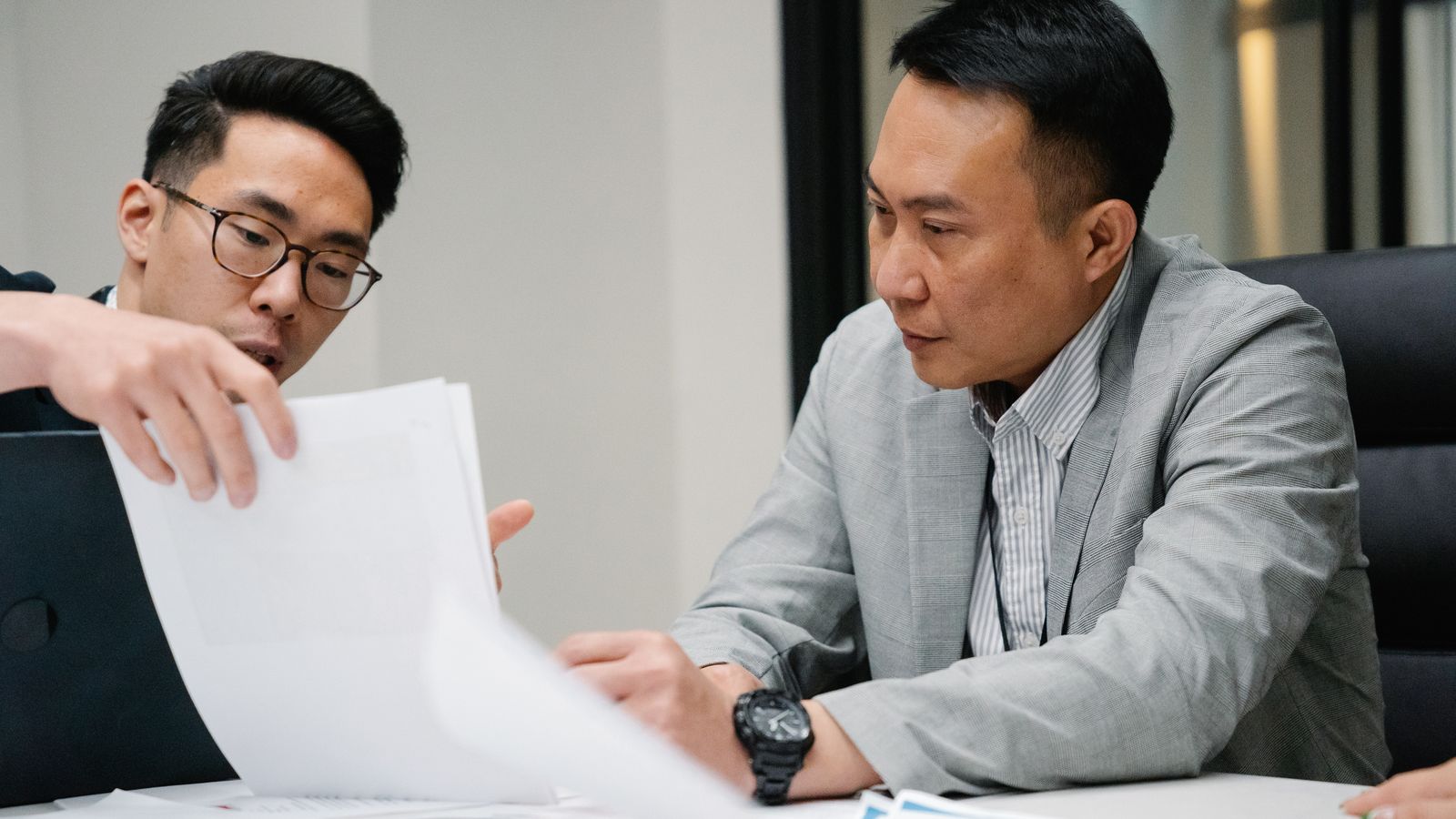 Two Thai lawyers in suits reviewing a contract together in a wood-panelled Bangkok office