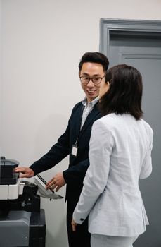 Two colleagues chatting by a copier in an office setting.
