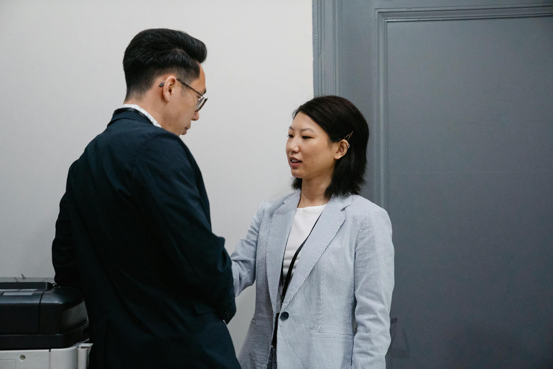 Man in Black Suit Talking a Woman in Gray Blazer