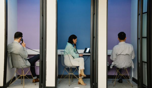 Business professionals using phone booths for communication in a modern office space.