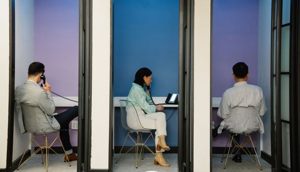 Business professionals using phone booths for communication in a modern office space.