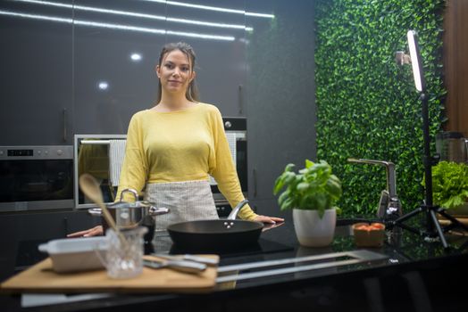 Woman in a sleek kitchen preparing food, surrounded by greenery and cookware.