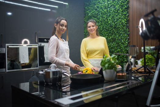 Two women cooking in a sleek kitchen with fresh ingredients and vibrant decor.