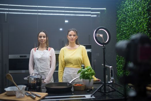 Two women filming a cooking vlog in a modern kitchen studio with professional equipment.