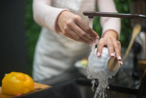 Free Close-up of hands washing a white bowl under a running faucet in a kitchen. Stock Photo