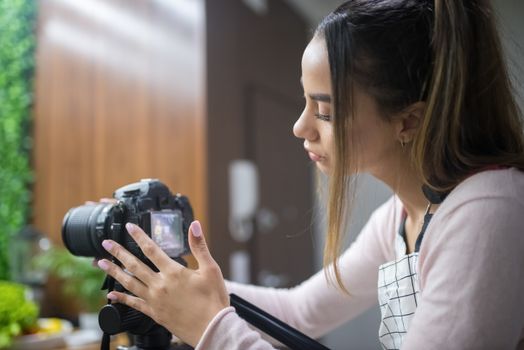 Focused woman adjusting DSLR camera in indoor setting, capturing a creative moment.