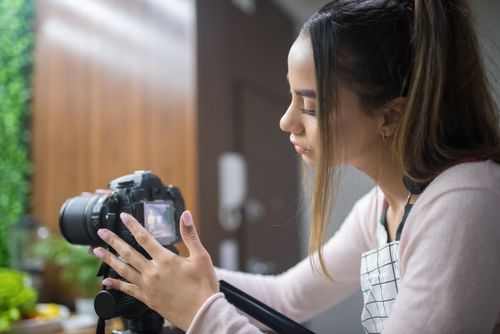 Free Focused woman adjusting DSLR camera in indoor setting, capturing a creative moment. Stock Photo