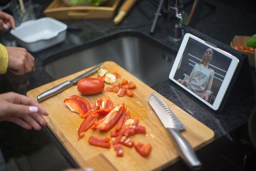 Hands preparing fresh vegetables on a chopping board with a digital tablet displaying a cooking video.