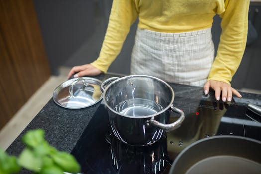 A woman in a yellow sweater cooking on an induction cooktop with a stainless steel pot.