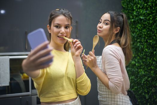 Two young women posing for a selfie in a modern kitchen, enjoying a fun cooking session.