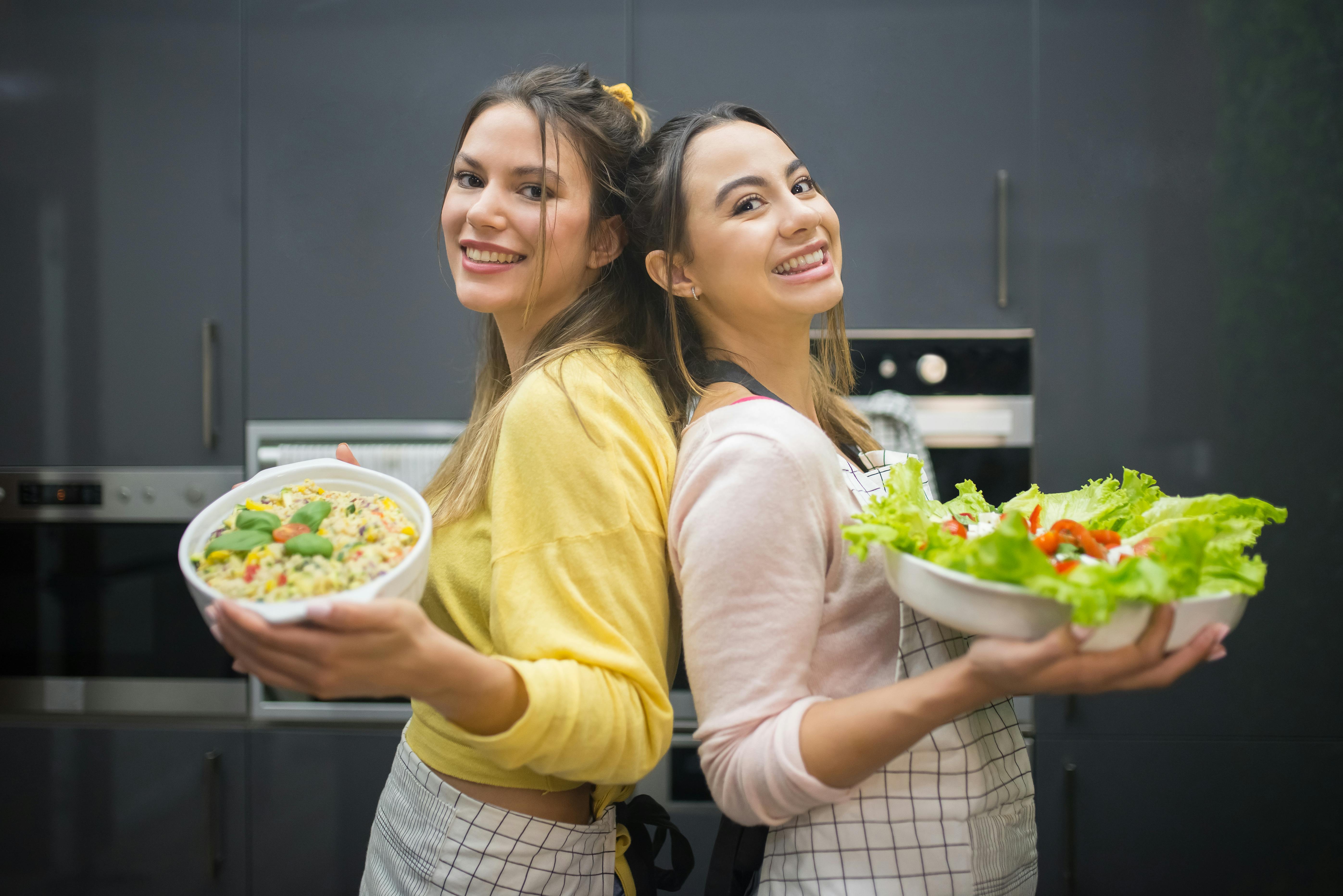 women standing back to back holding food platters