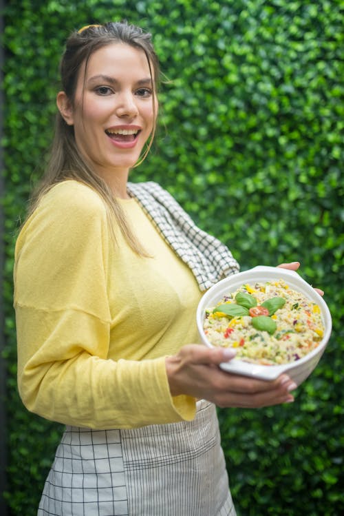 Woman in Yellow Long Sleeve Shirt Holding White Round Bowl with Food