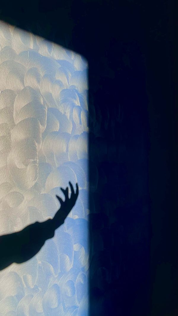 Uma sombra artística de uma mão alcançando uma parede texturizada com iluminação abstrata criando um efeito dramático.