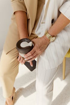 Close-up of hands holding a coffee tumbler in a professional setting, highlighting a wristwatch.