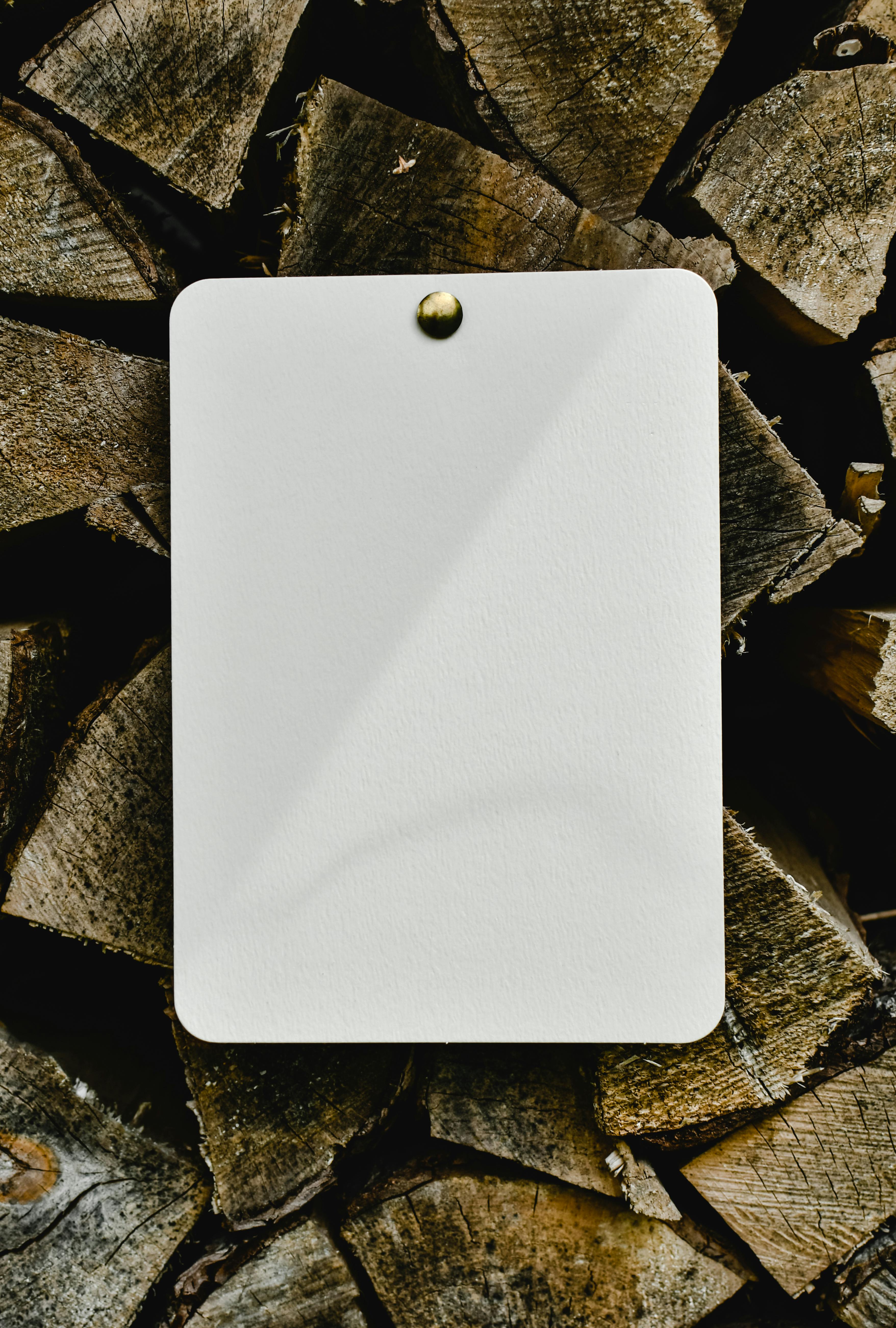 Vertical shot of blank white paper pinned on firewood stack, ideal for mockup or design use.