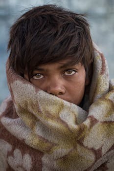 男孩裹着毯子在户外，一双富有表情的眼睛流露出天真和温暖