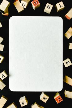 A blank white card surrounded by wooden alphabet blocks on a black background.