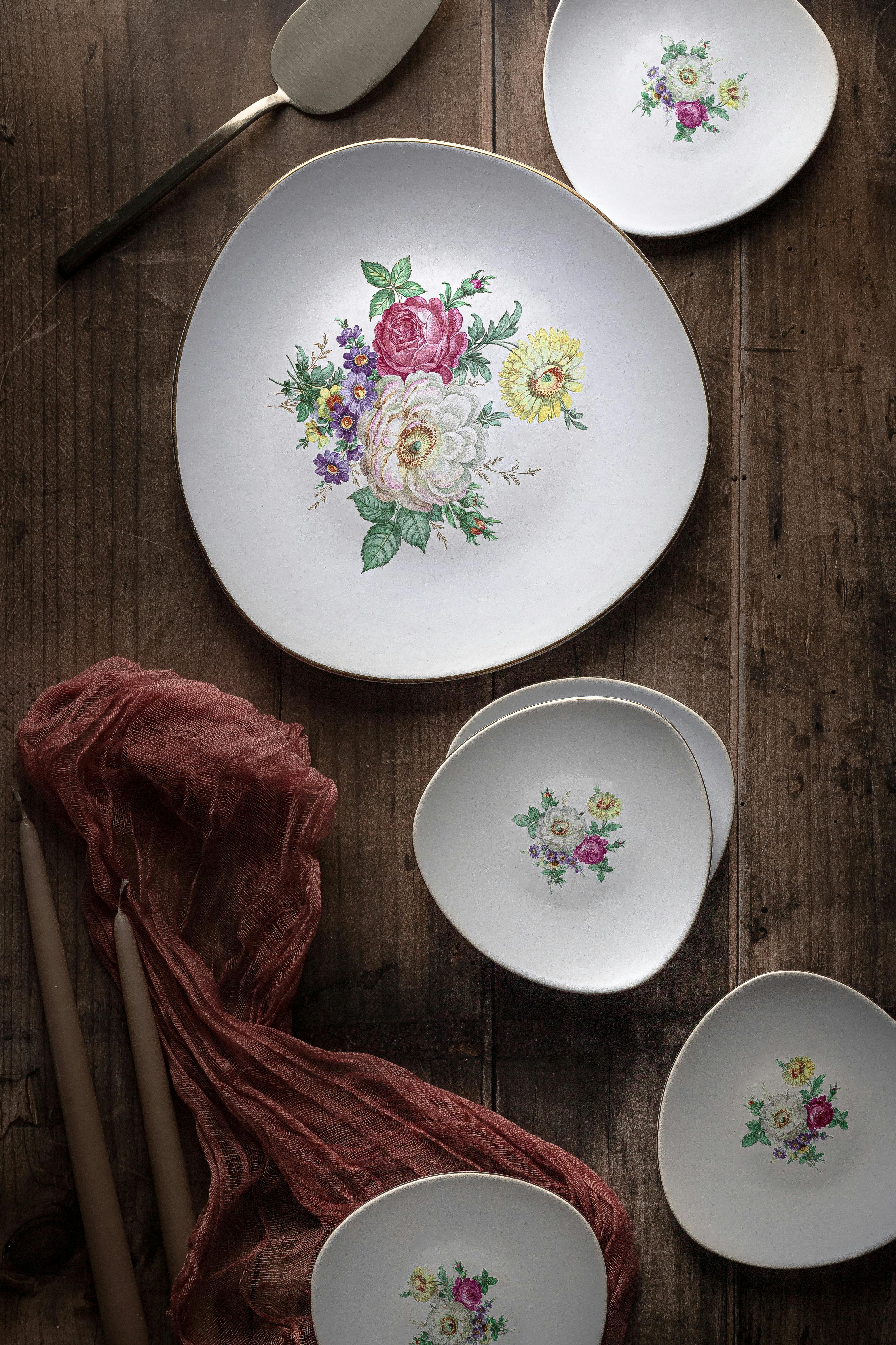 Overhead view of floral ceramic dinnerware arranged on a rustic wooden table with pink fabric and candles.